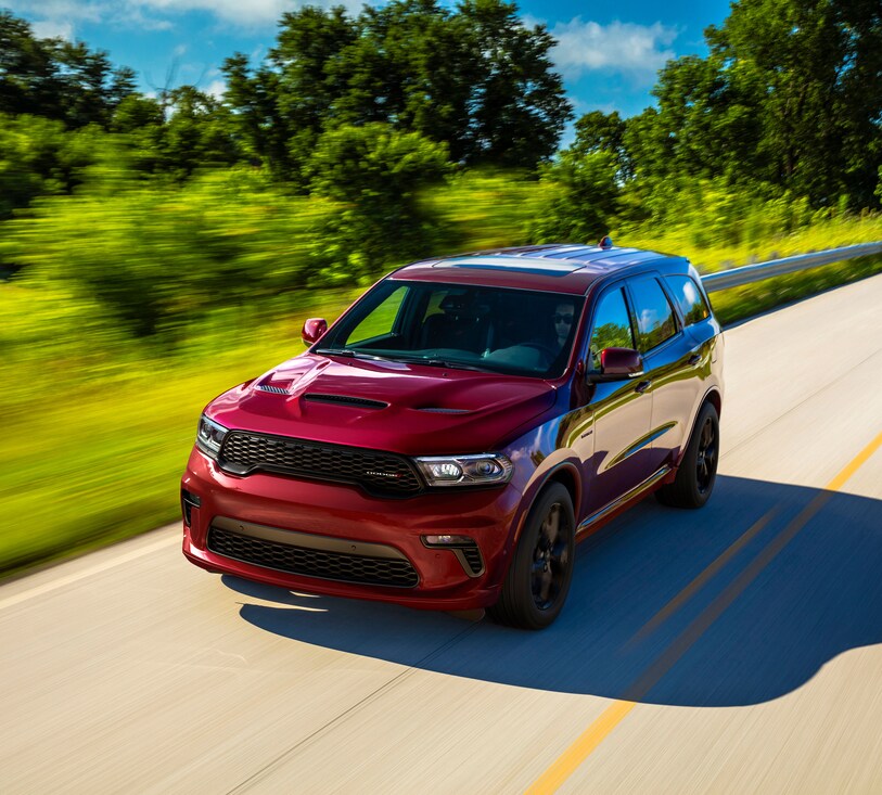 2023-Dodge-Durango-RT-SUV.png dark red Dodge Durango SUV driving past a blurred background of greenery