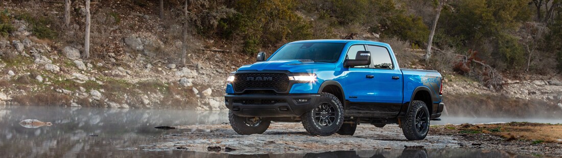 2025-RAM-1500-Rebel-CrewCab-Truck.png light blue Ram 1500 parked next to a stream