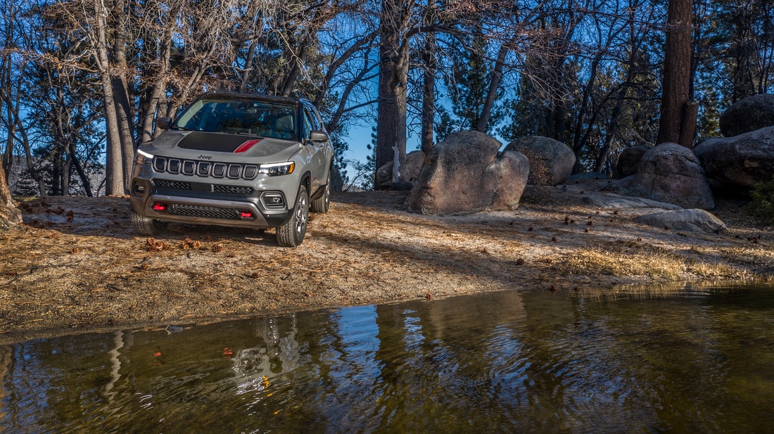 2023-Jeep-Compass-Trailhawk-SUV-L12.png dark grey Jeep Compass parked next to the water