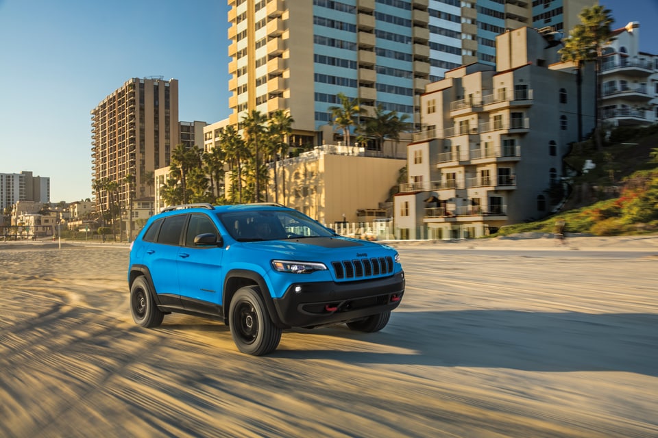 2020-Jeep-Cherokee-TrailHawk-WheelAddOn-SUV-L07.png bright blue Jeep Cherokee SUV driving on a beachfront