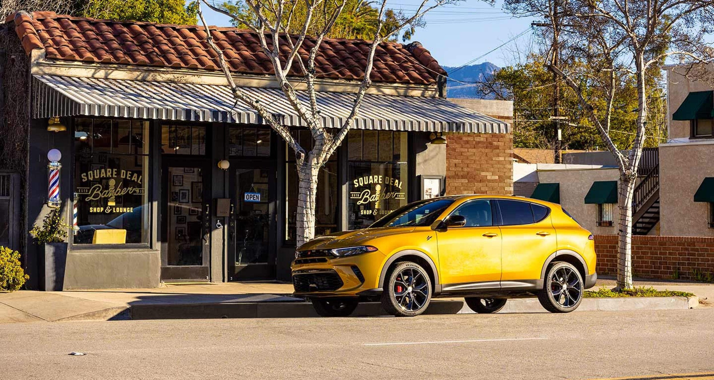 yellow Dodge Hornet in front of a barber shop