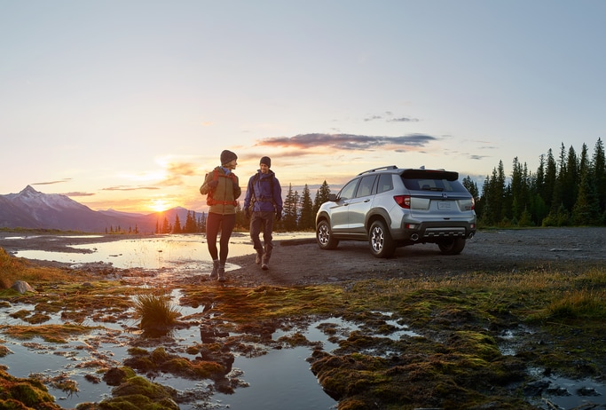 2023-Honda-Passport-TrailSport-SUV.png silver Honda Passport SUV parked with two people backpacking nearby