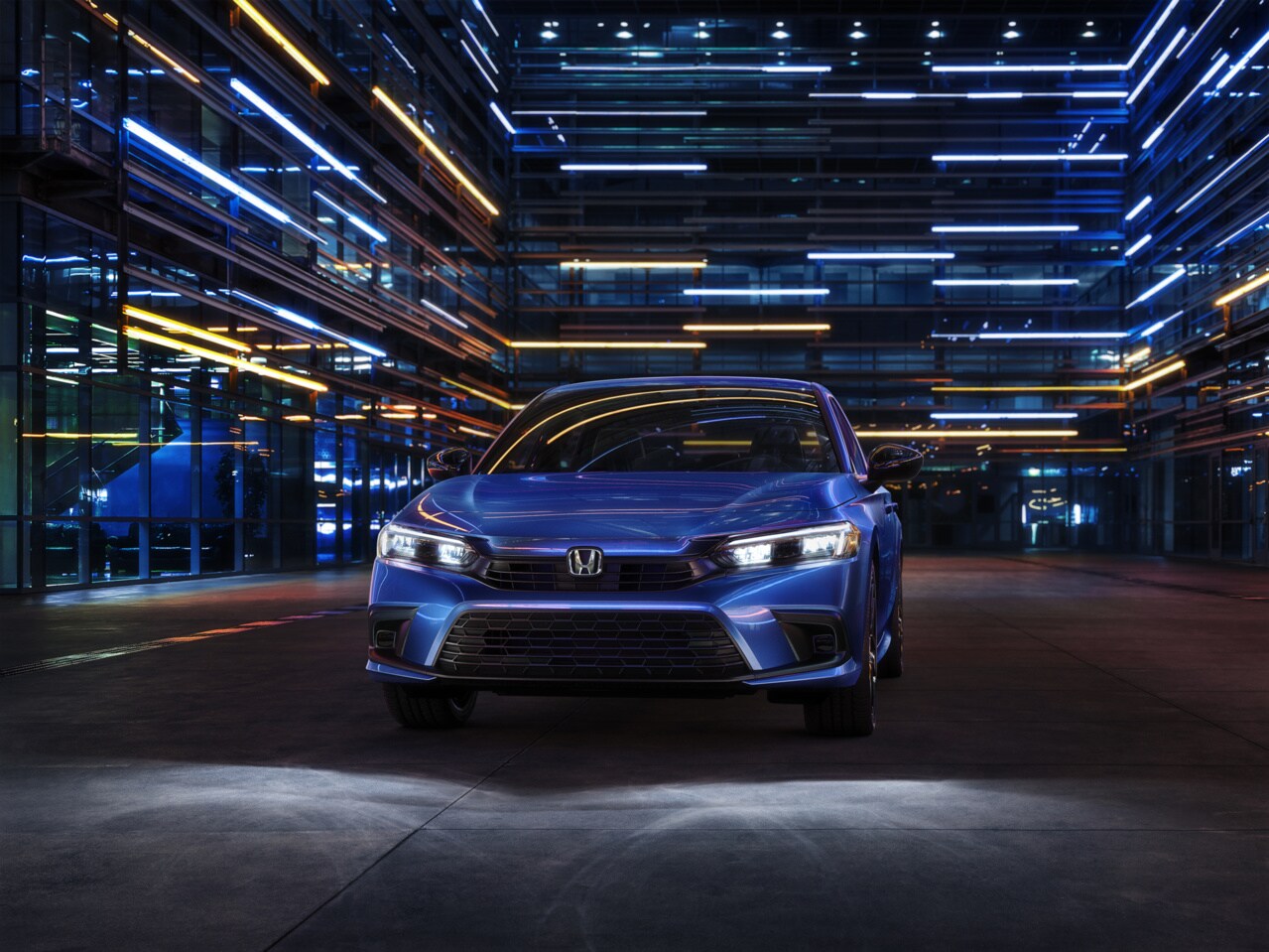 blue Honda Civic parked at night next to a modern, lit building