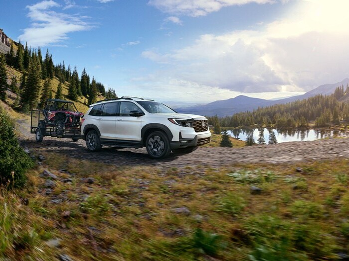white Honda Passport towing an ATV on a trail on a partially cloudy day