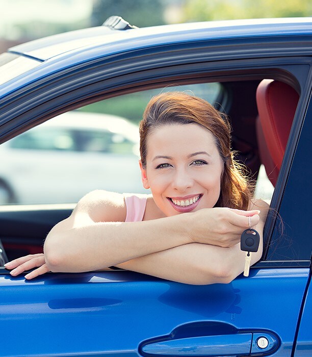 dealership-13.jpg woman in blue car holding the keys and leaning out the driver side window