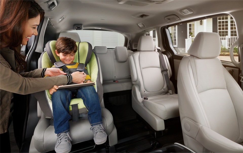 2022-Honda-Odyssey-Elite-Van-I01.png cream colored Honda Odyssey minivan interior, with driver buckling a child in a car seat into one of the captain's chairs
