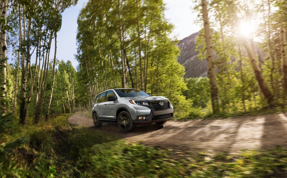 2021-Honda-Passport-Sport-SUV-L01.png silver Honda Passport SUV driving through a wooded trail