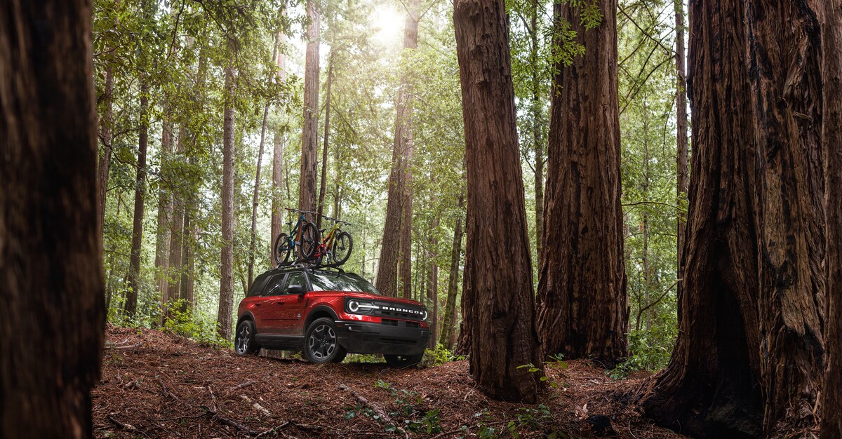 2023-Ford-BroncoSport-OuterBanks-SUV-L03.png red Ford Bronco Sport SUV parked in the woods with bikes on the roof rack
