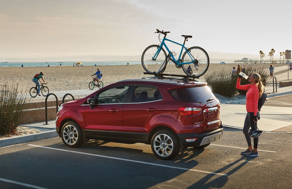 2021-Ford-EcoSport-Titanium-SUV-L03.png red Ford EcoSport SUV parked at a beach with a bike on the roofrack, hatchback visible