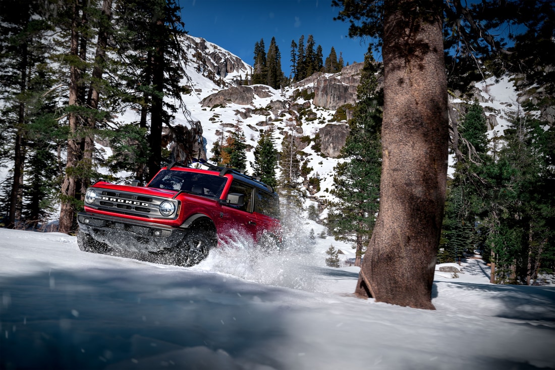 2023-Ford-Bronco-OuterBanks-2Door-SUV-L01.png red Ford Bronco driving at a steep angle on a snowy mountainside