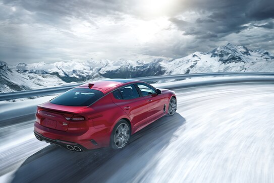 red Kia Stinger driving on the highway next to snowy
mountains