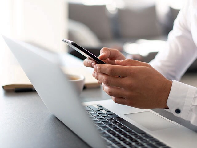 Contact our sales associates Hands holding a cell phone above a laptop on a wood table.