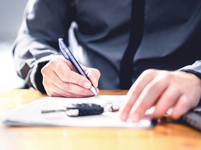 Sign the Paperwork - Lithia Nissan of Eugene Hand holding a pen about to sign a form. Car keys are sitting on the table.