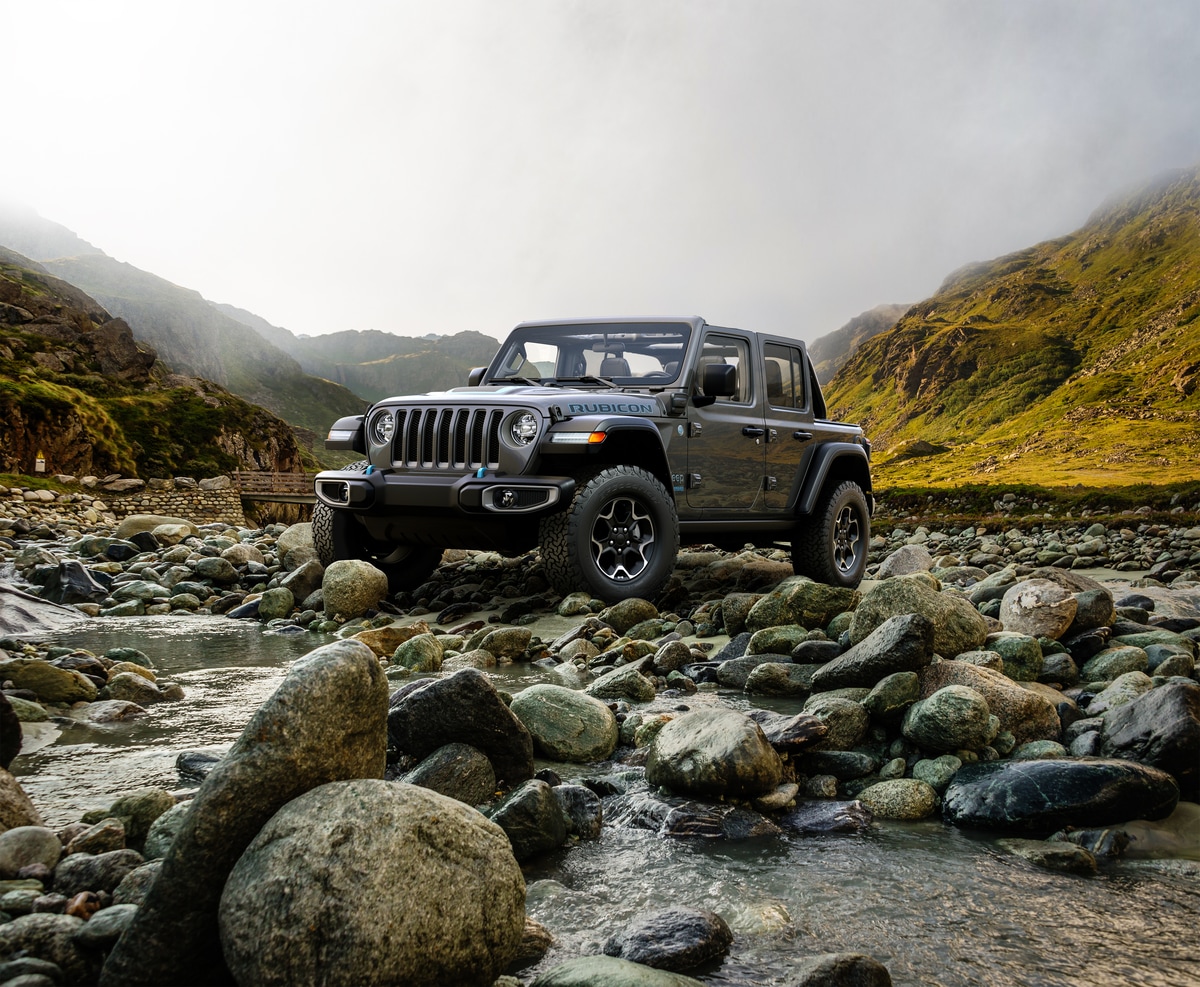 gray Jeep Wrangler 4xe bouldering over river rocks