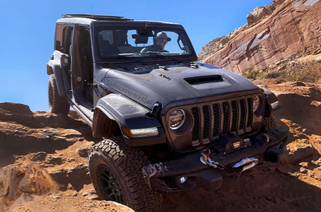 dusty grey Jeep Wrangler with the doors and roof off crawling down a steep desert hill