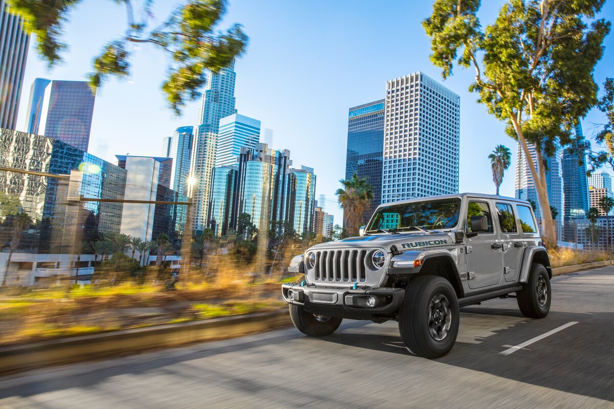 2022-Jeep-Wrangler-4XE-Rubicon-4x4-SUV-L07.png silver Jeep Wrangler SUV driving down a city street