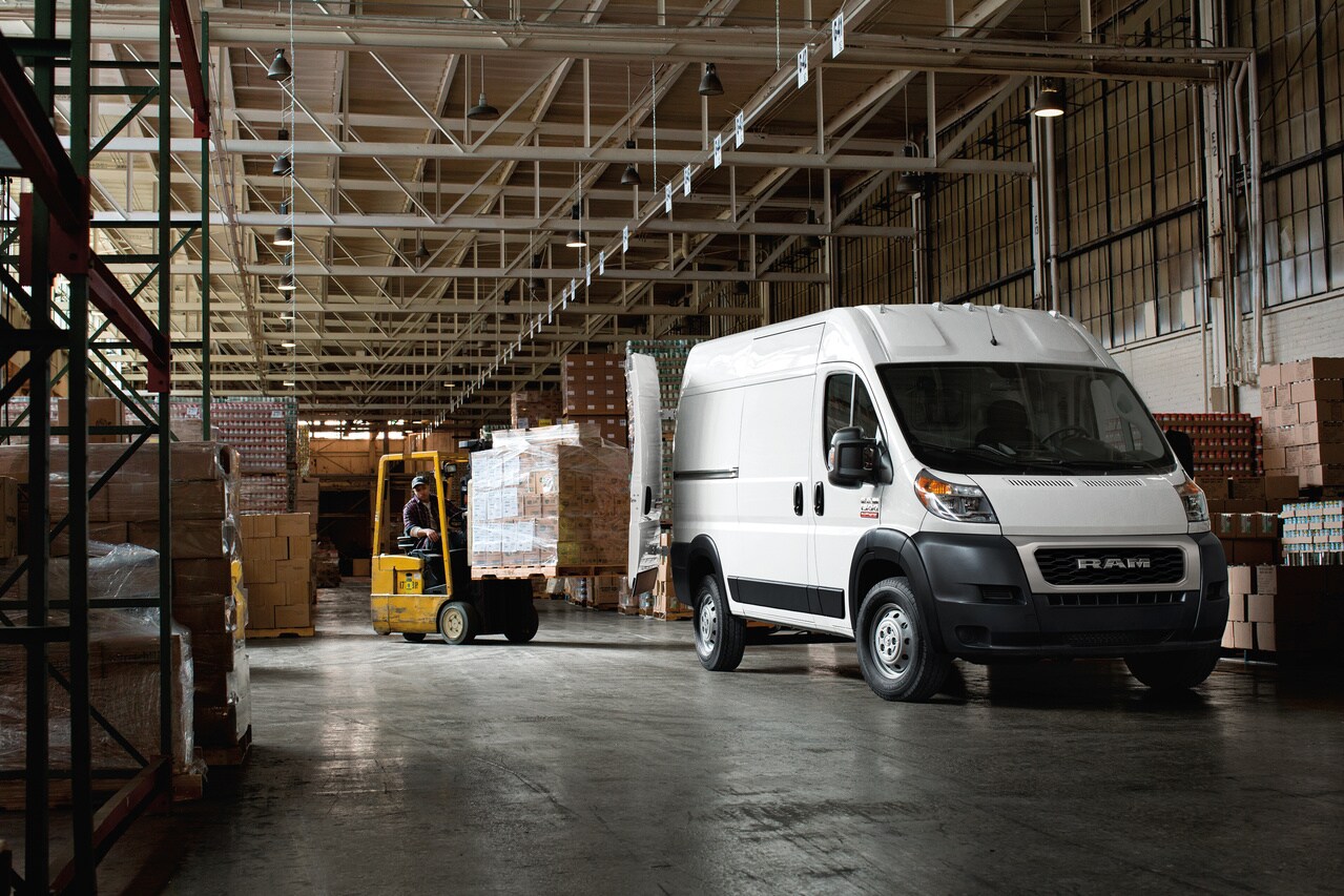 RAM Promaster 1500 white Ram ProMaster 1500 parked in a warehouse with a forklift of pallets driving towards it