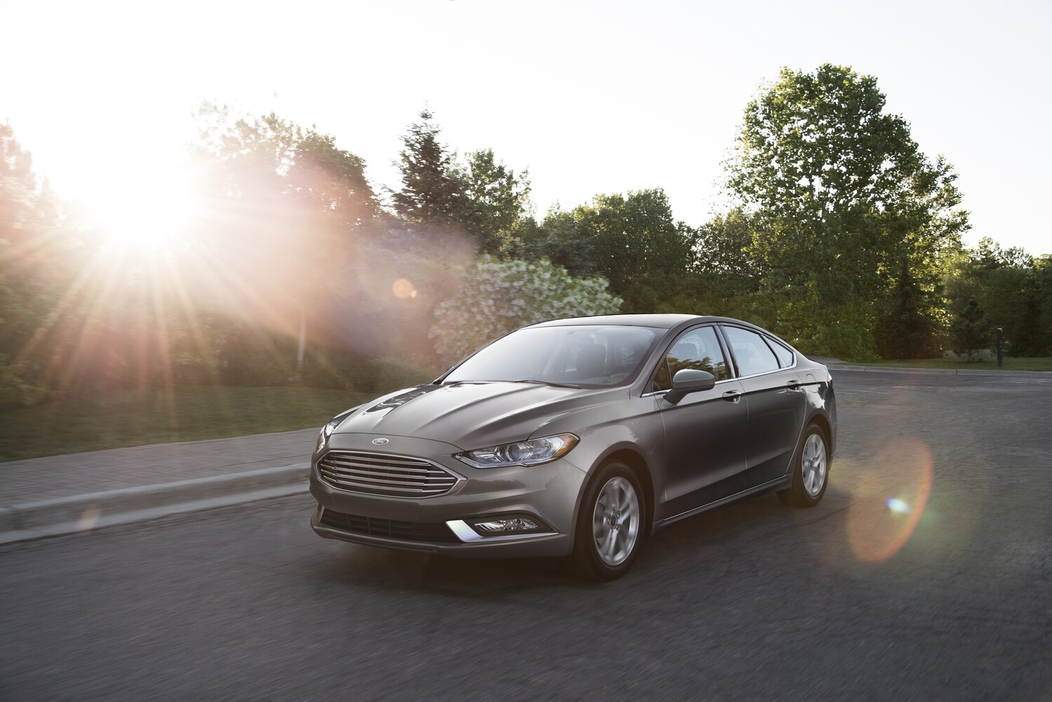 2018-Ford-Fusion-Titanium-Sedan-L03.png dark gray Ford Fusion sedan driving on a tree-lined street