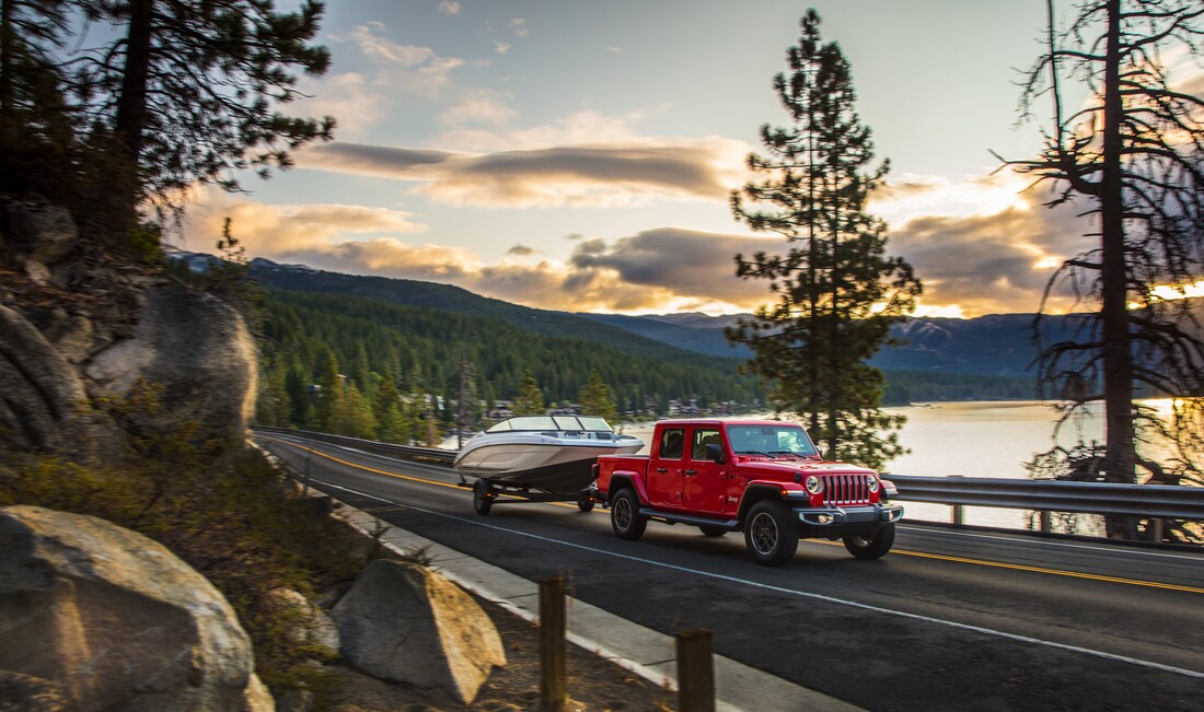2023-Jeep-Gladiator-Rubicon-Truck-L09.png red Jeep Gladiator truck driving down a wooded highway, next to a lake