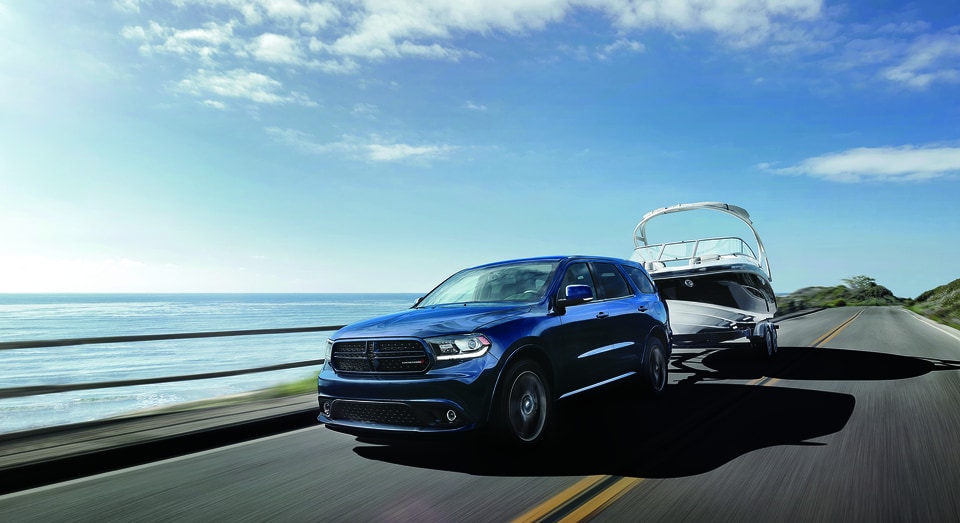 DDU17CA4_039 (2).png dark blue Dodge Durango SUV towing a boat near a coast
