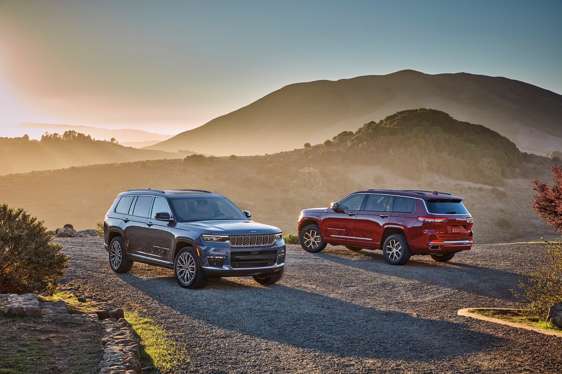 2021-Jeep-GrandCherokeeL-Lineup-02.png red and black Jeep Grand Cherokee L SUVs parked on a gravel road with hills in the background