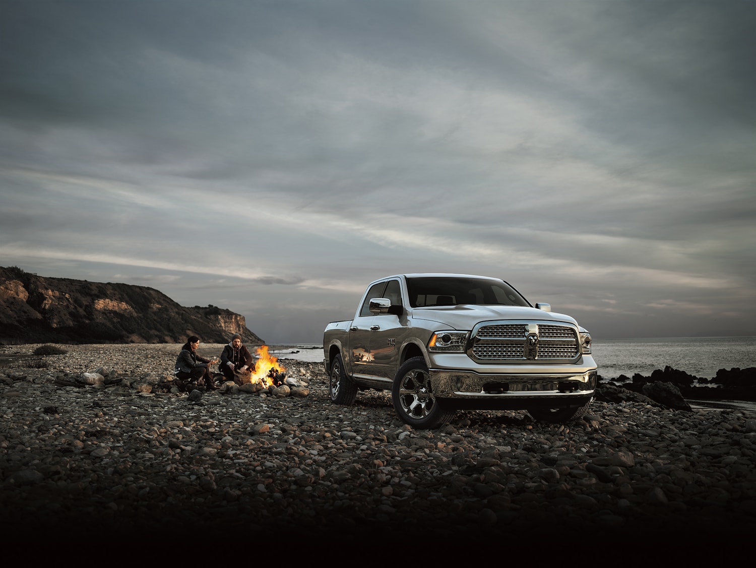 2015-Ram-1500-Laramie-CrewCab-MXM_DRP15US4_835_1500_XFEB_0116.png silver Ram 1500 truck parked on a beach with two campers next to a fire