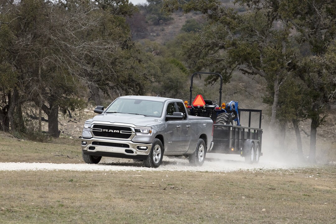 used silver Ram 1500 EcoDiesel truck towing a trailer on a dusty road
