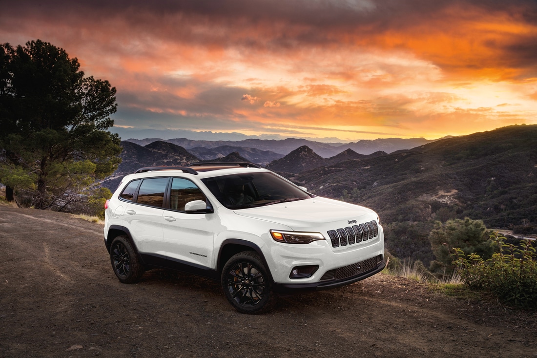 2023-Jeep-Cherokee-AltitudeLUX-SUV-L01.png white Jeep Cherokee SUV parked on a ledge at sunset