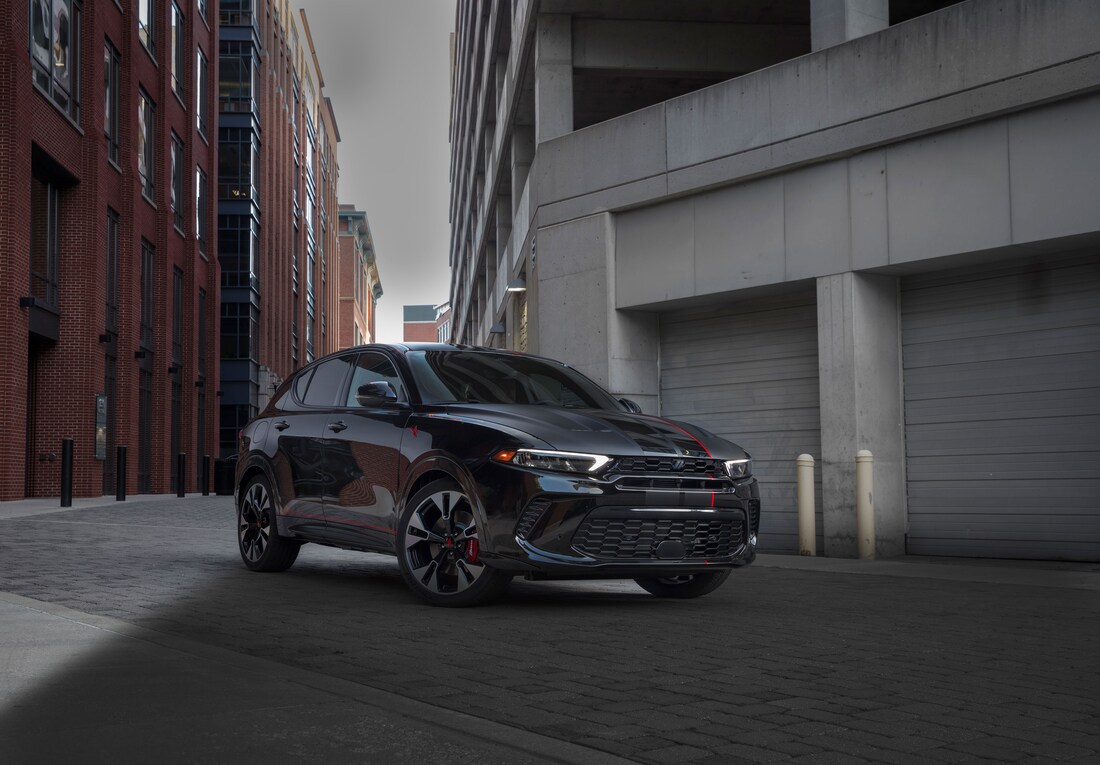 2023-Dodge-Hornet-SUV-L02.png black Dodge Hornet plug-in hybrid compact SUV parked in front of a set of garage doors