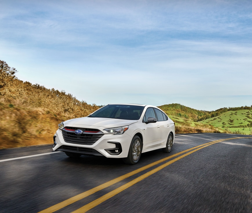 2023-Subaru-Legacy-Sport-SUV-L01.png white Subaru Legacy driving down a highway