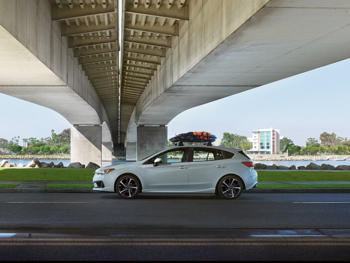 2022-Subaru-Impreza-Sport-Hatchback.png white Subaru Impreza sport hatchback parked underneath an overpass with gear on the roof rack