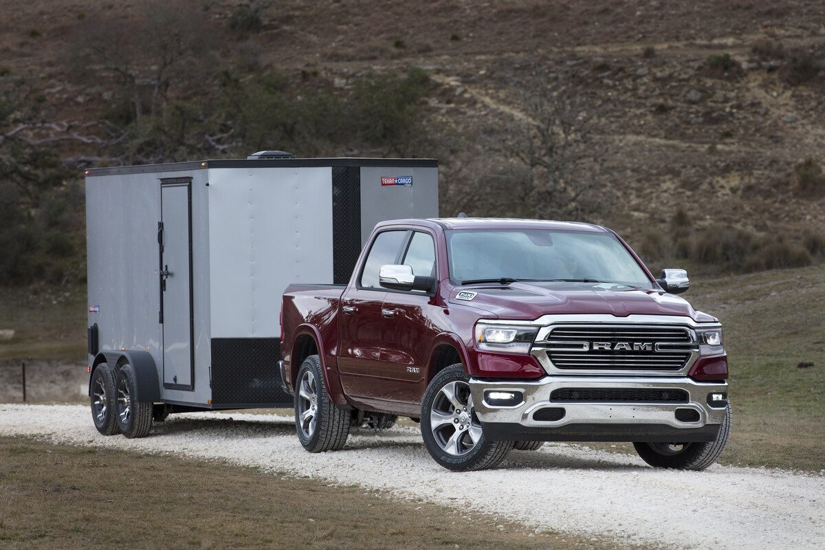 2023-RAM-1500-Laramie-CrewCab-WheelAddOn-Truck-L09.png maroon Ram 1500 truck towing a trailer down a dirt road