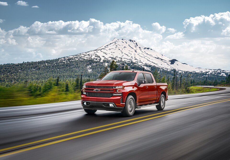 2020-Chevrolet-Silverado1500-RST-CrewCab-ShortBox-WheelAddOn-Truck-L02.png red Chevy Silverado 1500 truck driving down a highway with a mountain in the background