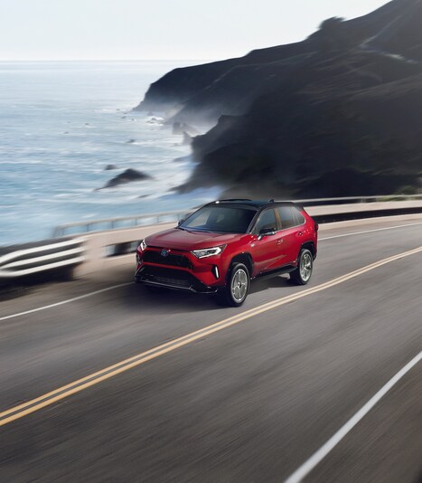 2023-Toyota-RAV4Prime-XSE-SUV-L06.png red Toyota RAV4 Prime plug-in hybrid SUV driving down a coastal road