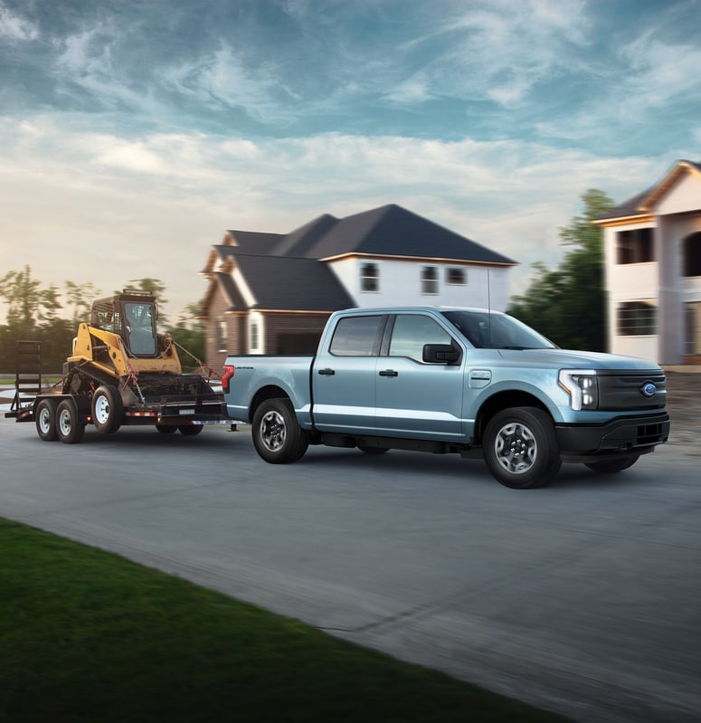 light blue Ford Lightning electric truck towing a trailer with a skid loader