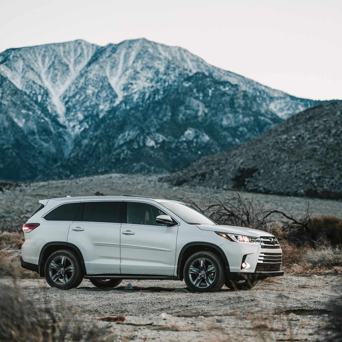 2021-Toyota-Highlander-Limited-SUV-L05.png white Toyota Highlander SUV parked on a dirt road, with a mountain in the background