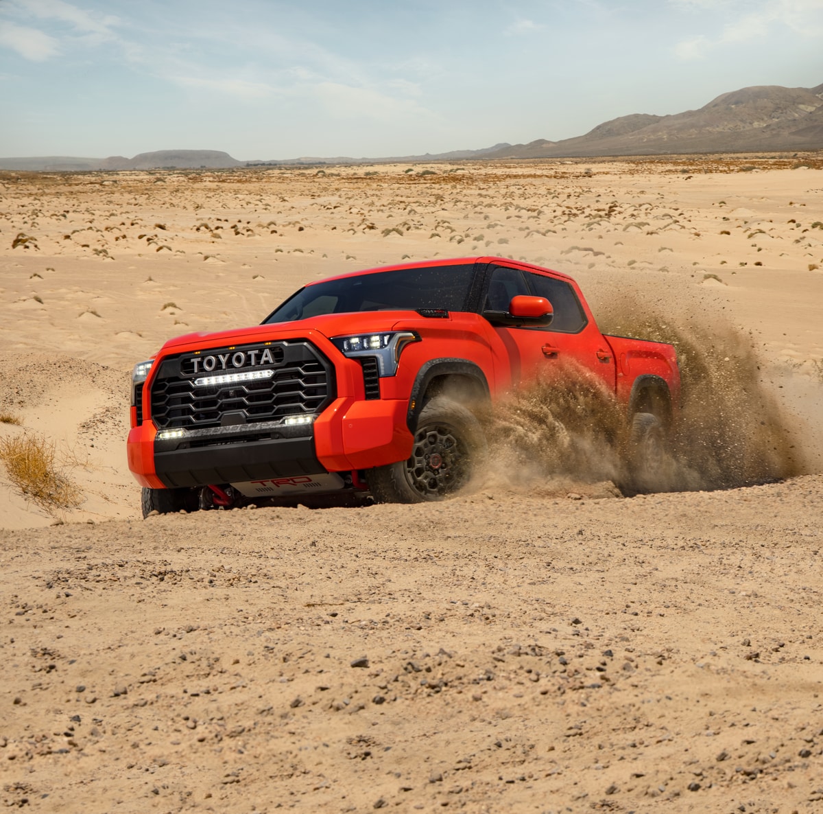 red Toyota Tundra truck kicking up sand on a desert trail