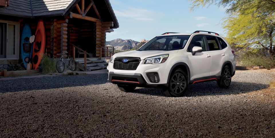 2020-Subaru-Forester-Sport-SUV-L01.png white Subaru Forester SUV parked in front of a rustic lodge