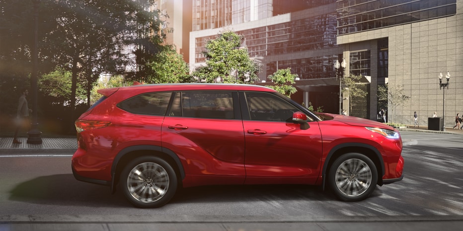 2023-Toyota-HighlanderHybrid-Platinum-SUV-L01.png red Highlander Hybrid SUV parked in a downtown area
