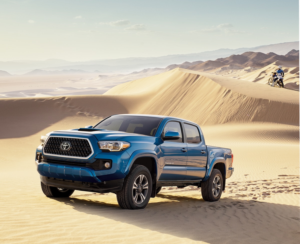 2018-Toyota-Tacoma-TRDSport-DoubleCab-Truck-L01.png blue Toyota Tacoma truck parked at a sand dune with a sport cyclist in the background