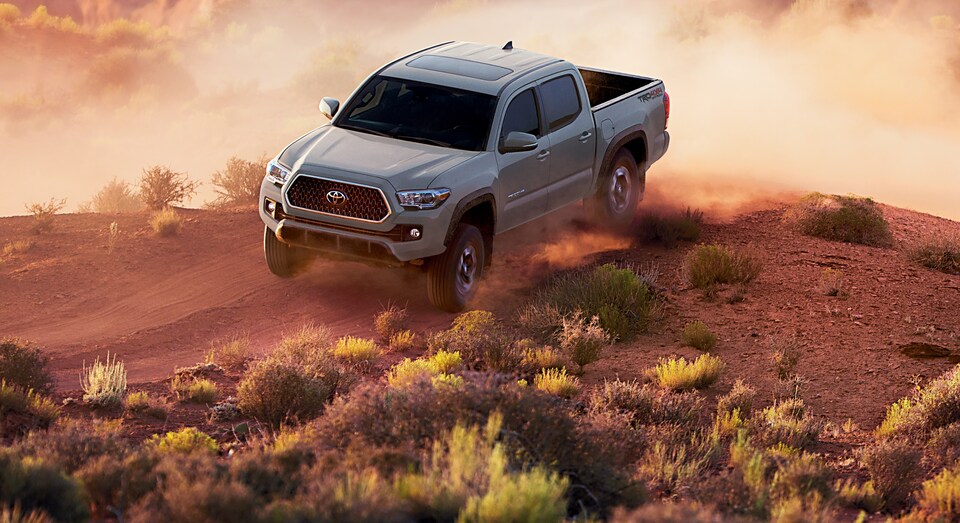 2018-Toyota-Tacoma-TRDOffRoad-DoubleCab-Truck-L06.png gray Toyota Tacoma truck cresting a dusty hill in the desert