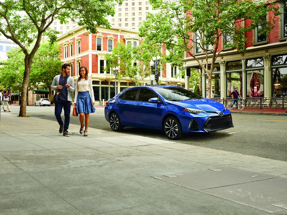 2016 Camry Blue.png blue Toyota Camry sedan parked on a city street under a tree