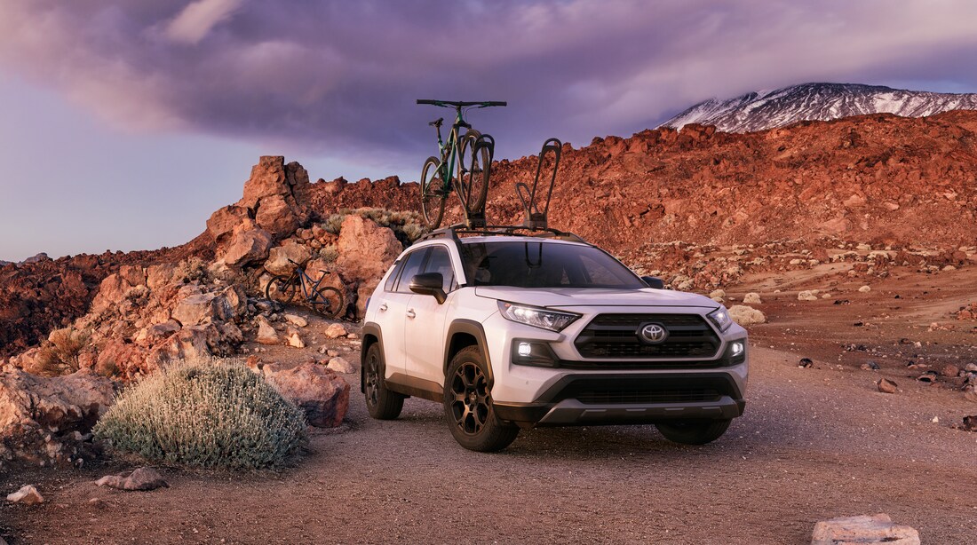 2023-Toyota-RAV4-TRDOffroad-SUV-L01.png white Toyota RAV4 TRD off-road parked in a rocky area with a bike on the top rack