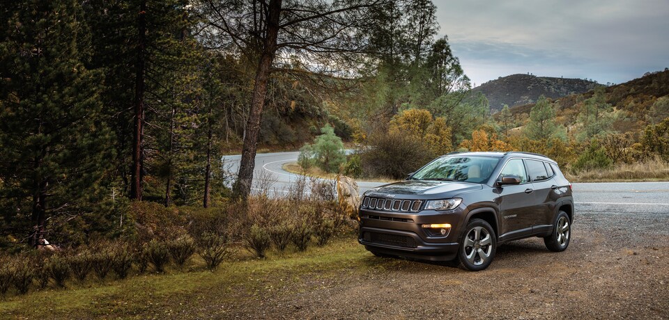 2021-Jeep-Compass-Latitude-SUV-L01.png dark gray Jeep Compass Latitude SUV parked next to a lake
