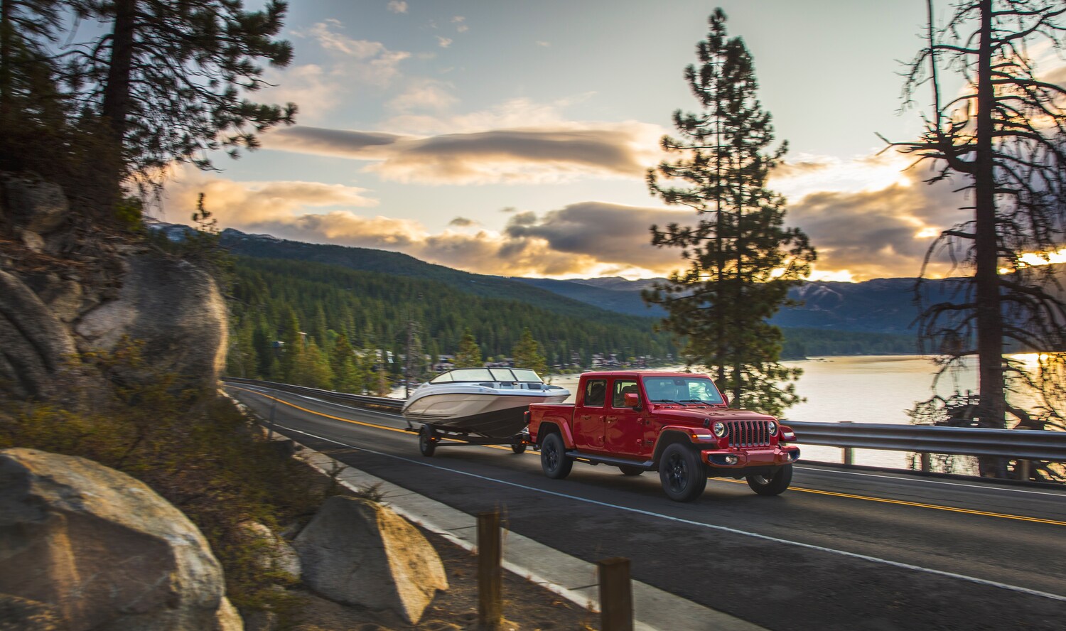 2021-Jeep-Gladiator-HighAltitude-Truck-L01.png red Jeep Gladiator truck towing a boat near a highway water over-look