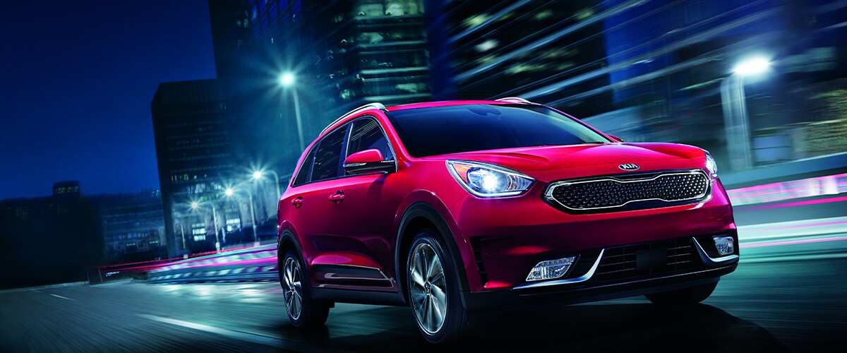Red Kia Niro driving through city at night