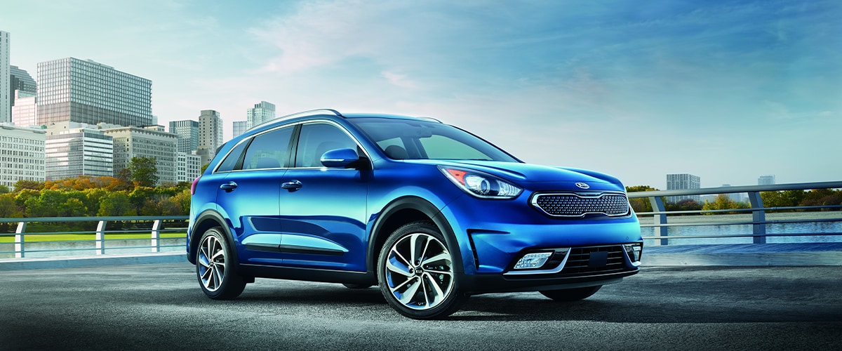 Blue Kia Niro parked in front of city skyline
