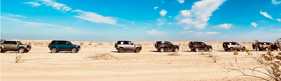 LINE UP OF SEVEN 2020 DEFENDER VEHICLES IN THE DESERT TERRAIN WITH BLUE SKYS IN THE DISTANCE