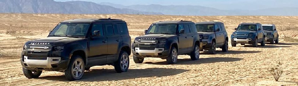CLOSE UP LINE UP OF FIVE 2020 DEFENDER VEHICLES IN THE DESERT TERRAIN WITH MOUNTAINS IN THE BACKGROUND