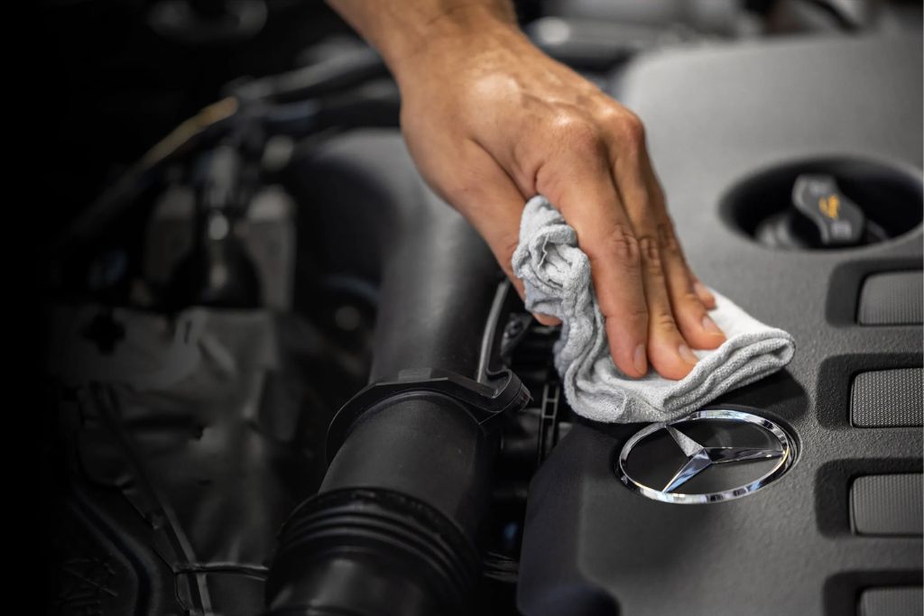 Close-up shot of a hand using a rag to wipe under the hood of a Mercedes Benz car
